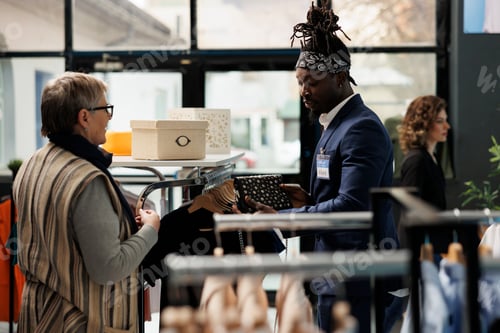 Preview: Boutique worker helping senior client choosing black bag