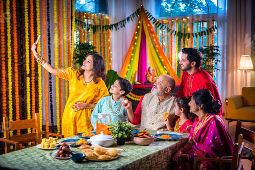 Preview: Portrait of happy Indian family in traditional outfit celebrating Diwali at home eating food