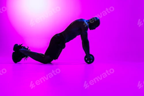 Preview: Bodybuilder working on his abs with a ab roller on studio background with color filter
