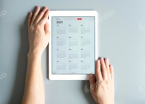 Preview: a tablet with an open calendar for 2021 year in a womans hands on a gray background