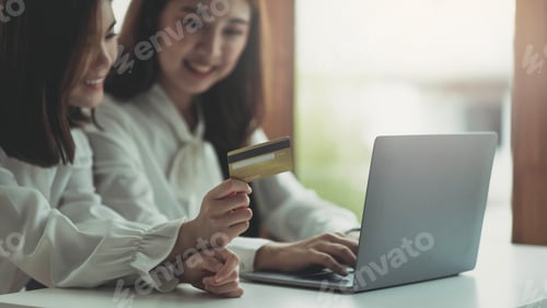 Preview: Two young asian women holding credit card and using laptop computer for shopping on line with
