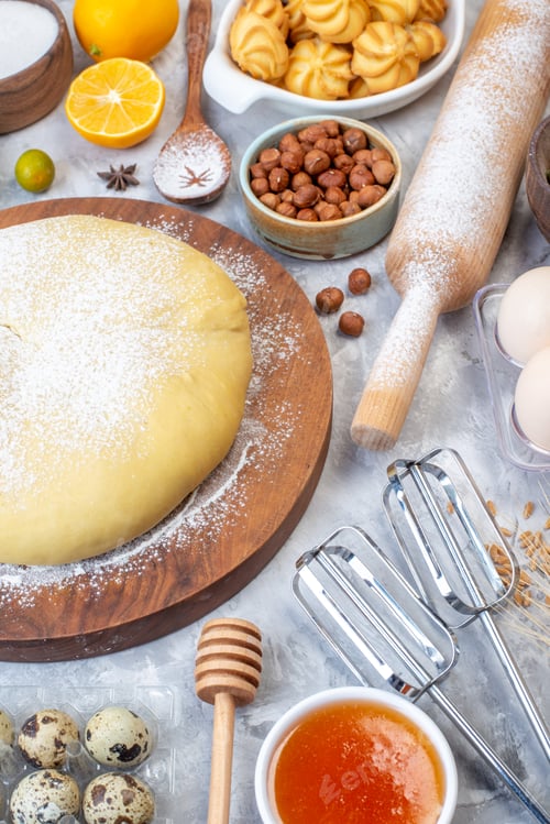 Preview: Overhead view of raw pastry on round board and set of various foods grater on ice background