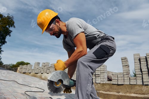 Preview: Slicing by circular saw. Male worker in yellow colored uniform have job with pavement