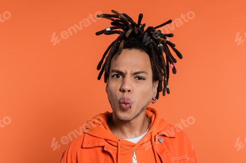 Preview: portrait of pierced multiracial man with dreadlocks pouting lips isolated on coral background
