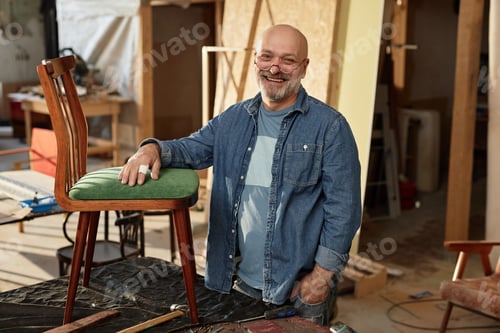 Preview: Smiling senior craftsman looking at camera in furniture restoration workshop