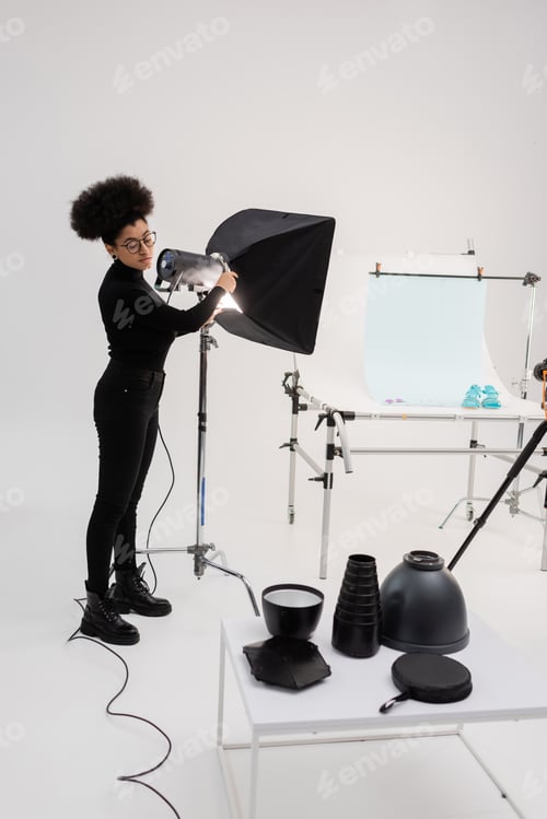 Preview: african american content maker assembling floodlight near shooting table and lighting equipment in