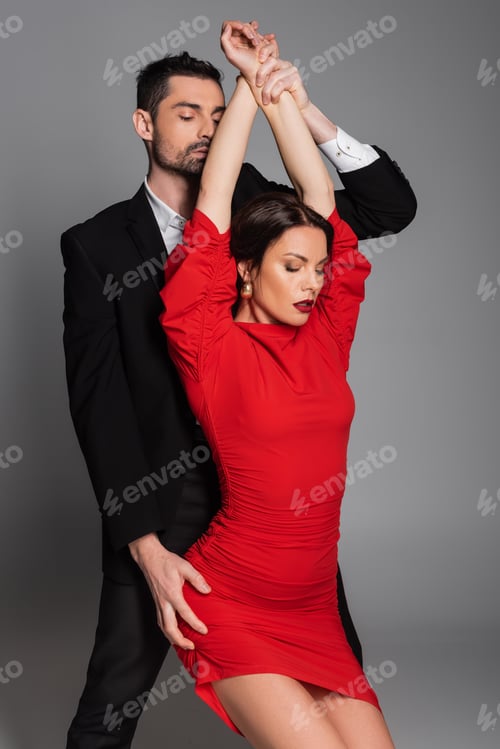 Preview: Bearded man touching hands and hip of sexy girlfriend in red dress isolated on grey