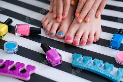 Preview: Children's feet with bright pedicure and manicure of colors and bottles of bright nail polish.