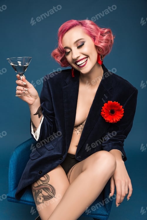 Preview: happy tattoed girl in jacket with boutonniere and wineglass infront of blue background