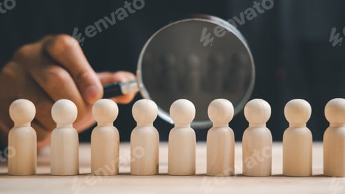 Preview: A hand holding a magnifying glass over a row of wooden figurines. The magnifying glass focuses on