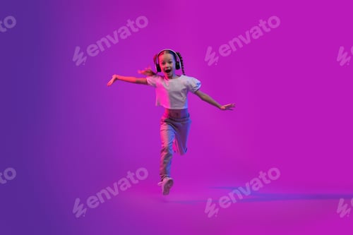 Preview: Excited little girl with wireless headphones running on colorful background