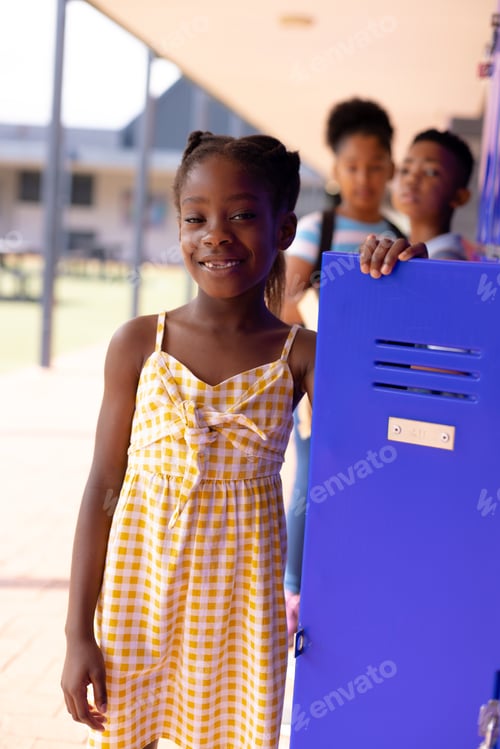 Preview: Portrait of happy african american schoolgirl standing next to locker at school