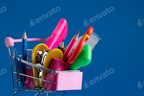 Preview: Close up of miniature shopping trolley with school materials and copy space on blue background