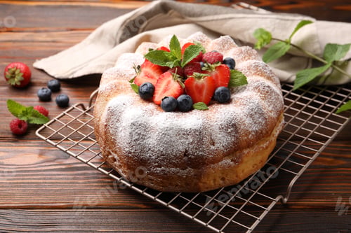 Preview: Tasty Bundt cake with powdered sugar and berries on wooden table, closeup