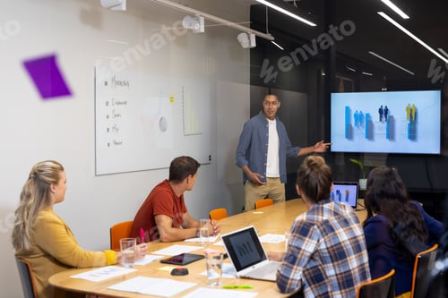 Preview: Biracial male creative making presentation at screen to diverse colleagues in meeting room