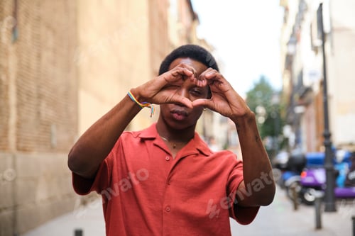 Preview: Gay black man in a red shirt holding his hands together in the shape of a heart.