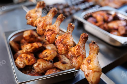 Preview: Fried chicken legs on a metal skewer in the kitchen.