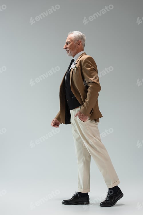 Preview: full length of happy middle aged groom in suit with floral boutonniere standing with hand in pocket