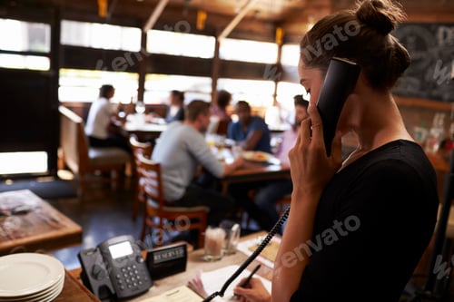 Preview: Young woman taking a reservation by phone at a restaurant