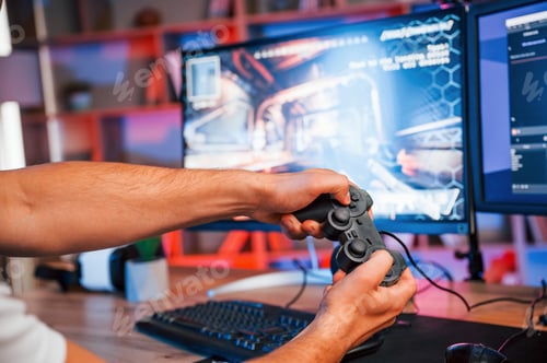 Preview: Close up view of hands with joystick controller. Male game streamer in casual clothes is indoors