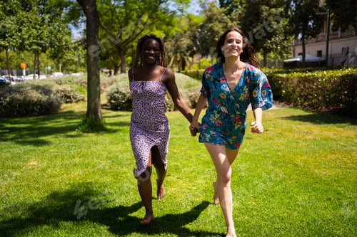 Preview: Two women of different ethnicities running holding hands outdoors