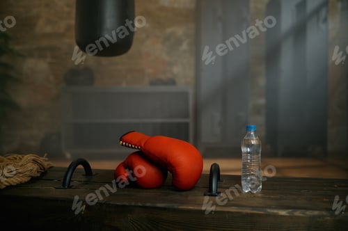 Preview: Boxing red gloves, plastic bottle of water and punching bag at sport gym