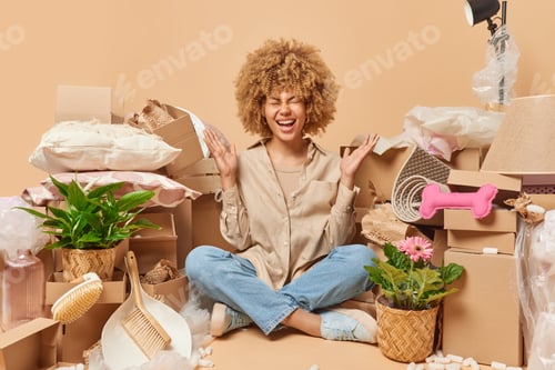 Preview: Happy overjoyed curly haired young woman exclaims loudly keeps palms raised up smiles broadly being