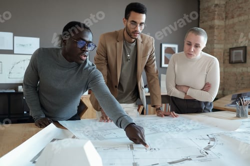 Preview: Young confident architect pointing at sketch on blueprint