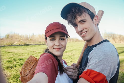 Preview: Portrait of smiling young couple with baseball equipment in park