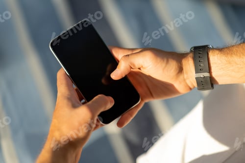 Preview: Cropped of male hands using smartphone, blurred outdoor background