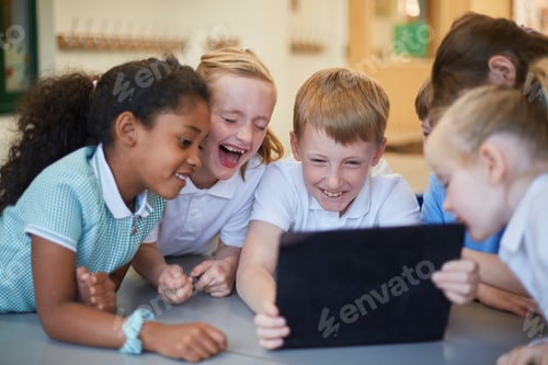 Preview: A group of joyful schoolchildren laughing and looking at a tablet screen together.