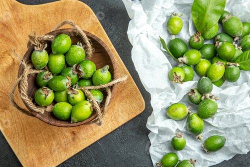 Preview: Above view of natural fresh green feijoas in a small brown pot on wooden cutting board and white