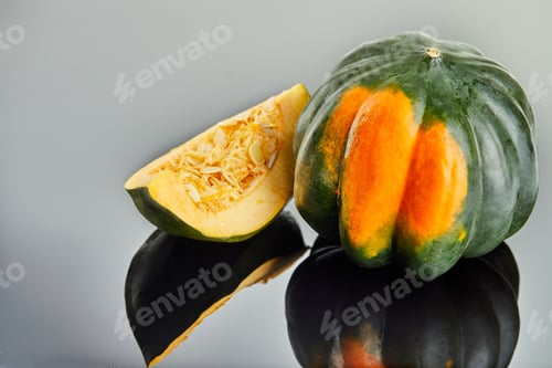 Preview: Green-orange chestnut pumpkin and a sliced slice of pumpkin lying on a gray background