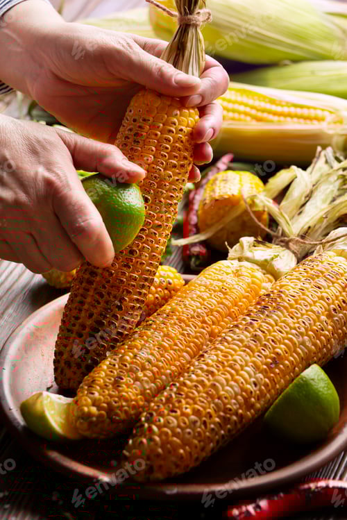 Preview: Female hands rubbing a roasted sweet corn cob with lime