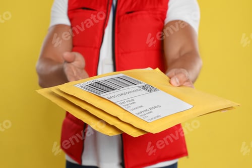 Preview: Young courier with envelopes on yellow background, closeup