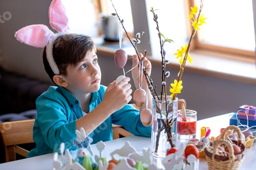Preview: a boy with hare ears decorates willow branches with Easter eggs