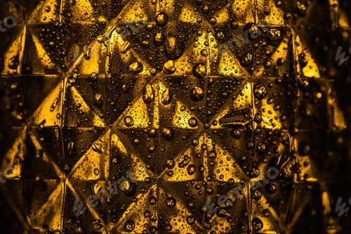 Preview: Close up View of Geometric Faceted Glass With Yellow Illumination in Dark