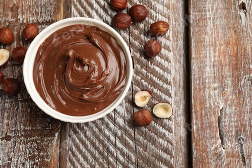 Preview: Chocolate hazelnut spread in bowl and nuts on wooden table, flat lay. Space for text