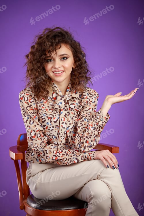 Preview: Happy curly-haired girl sitting on a chair and smiling