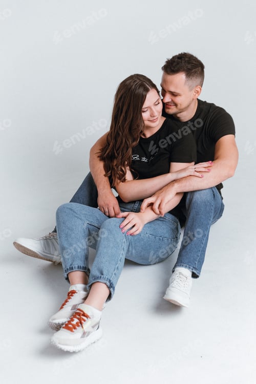 Preview: A young couple in love is sitting on a white background hugging and smiling