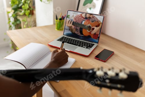 Preview: African teenage girl watching online course on laptop while playing the guitar