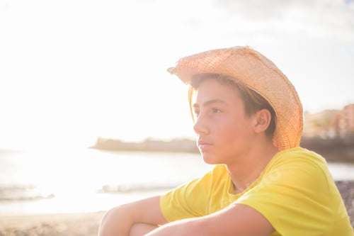 Preview: young beautiful boy 15 years old sitting on the beach in vacation looking at the horizon