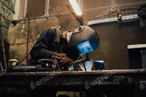 Preview: Worker in a welder mask works in a workshop for welding iron. Man makes iron products.