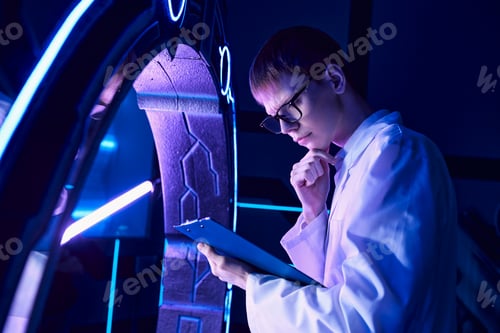 Preview: futuristic science, discovery center, young scientist with clipboard thinking at innovative device