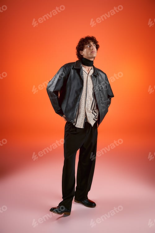 Preview: Stylish young man poses confidently against vibrant orange backdrop showcasing modern fashion flair