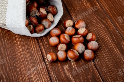 Preview: side view of hazelnuts in shell scattered from a sack on wooden background