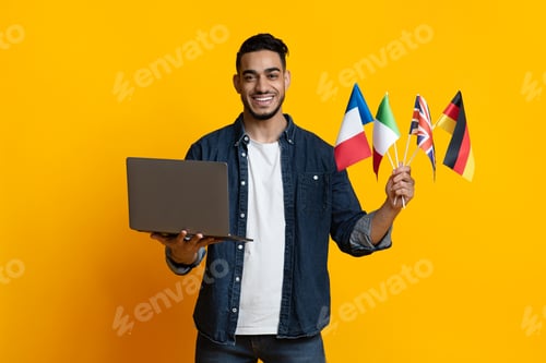 Preview: Cheerful arab guy holding laptop and international flags on yellow