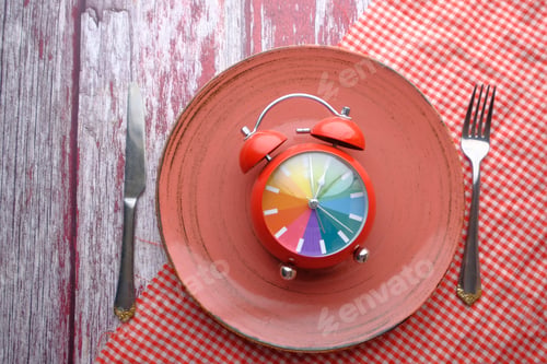 Preview: A vibrant and colorful alarm clock beautifully placed on a plate accompanied by cutlery
