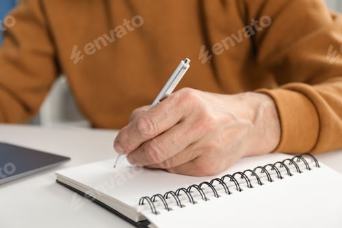 Preview: Senior man taking notes while learning online at desk indoors, closeup. Self-study