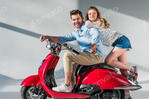 Preview: side view of stylish young couple on red scooter looking at camera